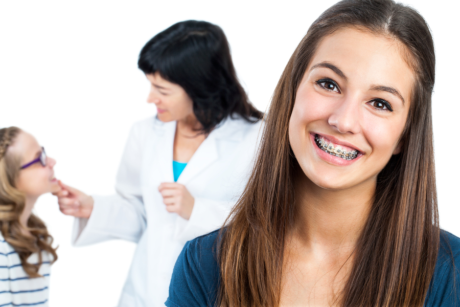 girl smiling with braces, orthodontist in background with patient. Katy, TX braces